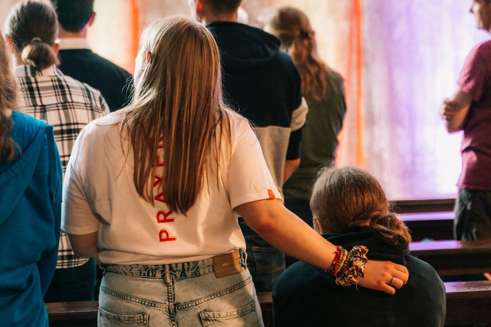 A young woman wearing a prayer t-shirt with her arm around another worshipper during a service