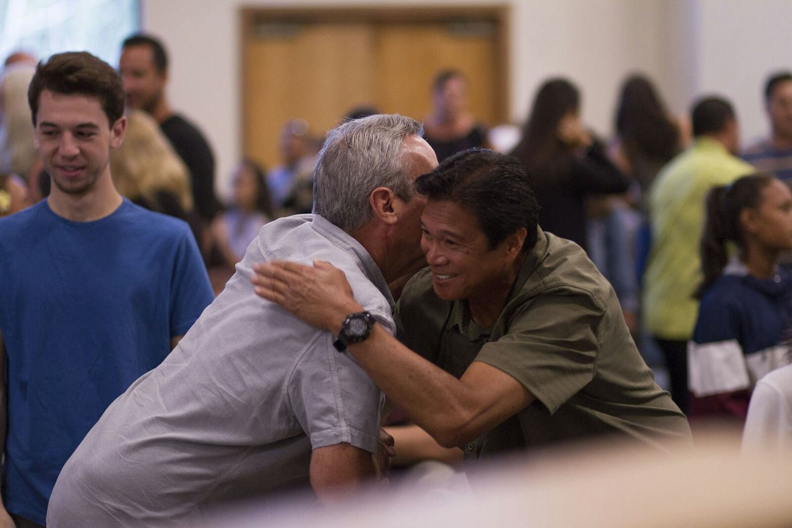 Two men greeting each other with a hug in a busy church foyer